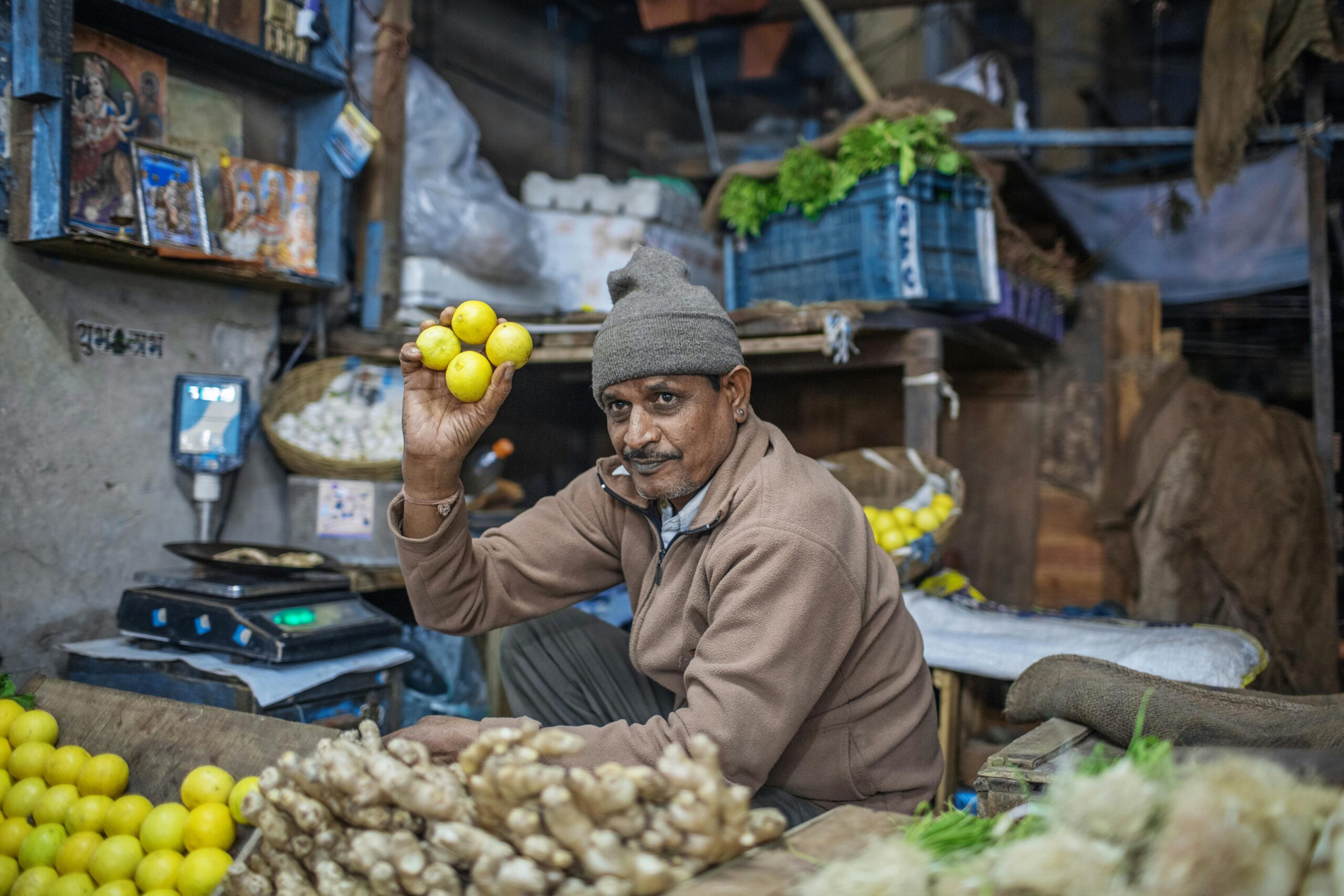 Adult Indian man in warm clothes selling bright lemons while owning small local stall with fruit and vegetable